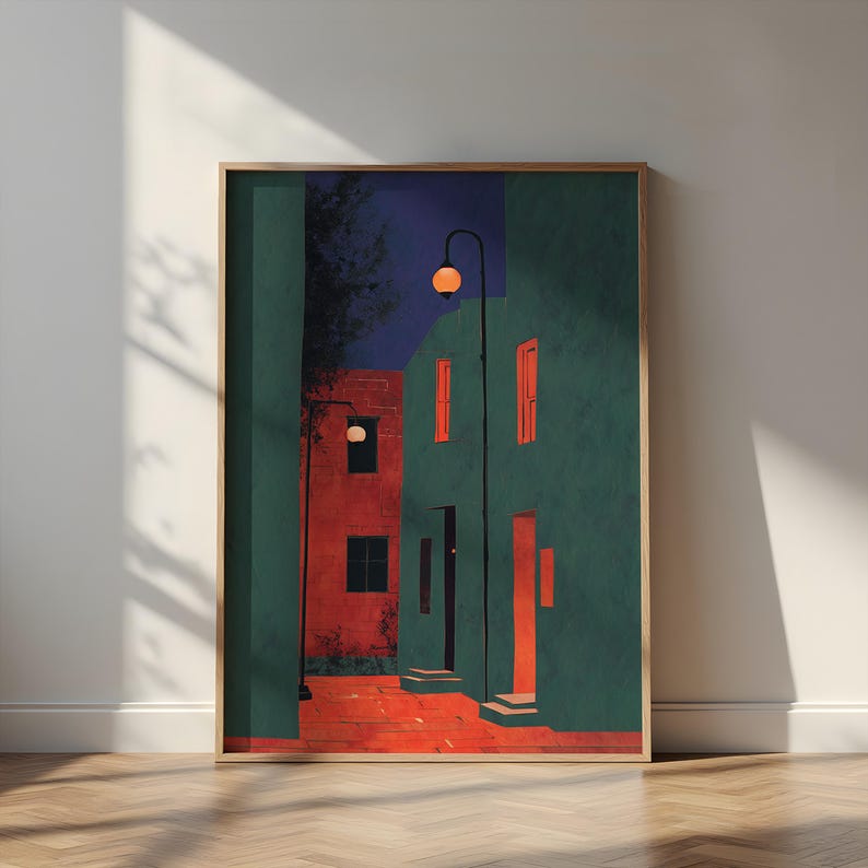 以下が含まれることがあります： ティールと赤の色合いの建物が描かれた街並みのシーンを描いた、額装されたアートプリント。このアートワークは、街灯と濃い青色の空がある夜のシーンを特徴としています。プリントは木製の床に展示されています。