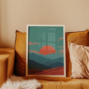 May include: A framed art print featuring a landscape scene with a large orange sun setting over layered blue mountains and red hills. The artwork is displayed on a mustard-colored couch with pillows.