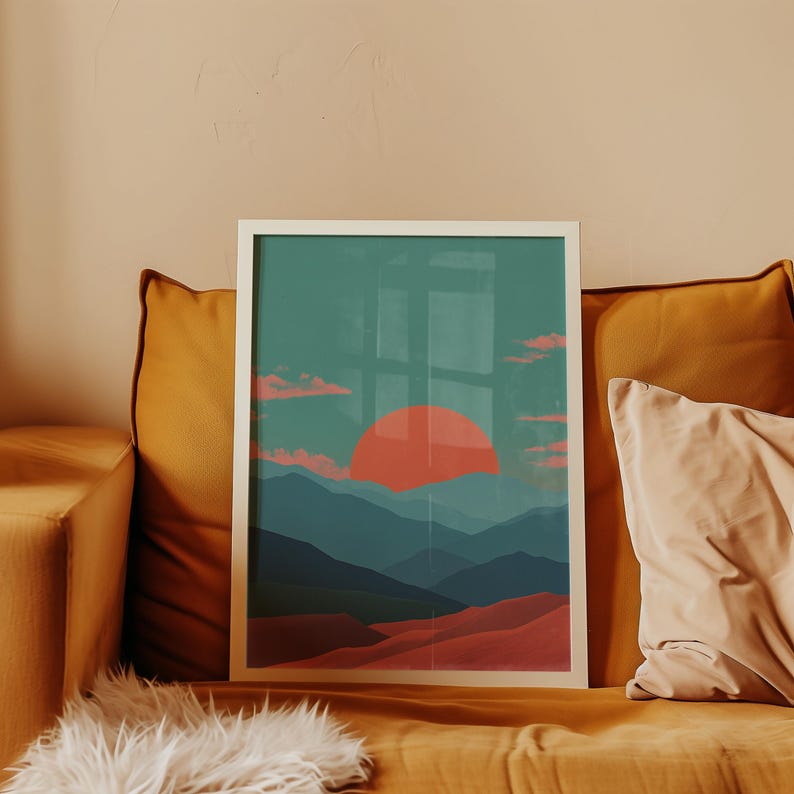 May include: A framed art print featuring a landscape scene with a large orange sun setting over layered blue mountains and red hills. The artwork is displayed on a mustard-colored couch with pillows.