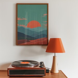May include: A framed landscape art print with a sunset over layered blue mountains. An orange lampshade sits atop a beige lamp base. A vintage record player with a black vinyl record is on a wooden surface.