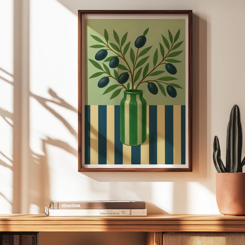 May include: A framed art print featuring a still life of olive branches in a green and white striped vase. The background has a striped pattern in blue and yellow. The artwork is displayed on a wooden surface.