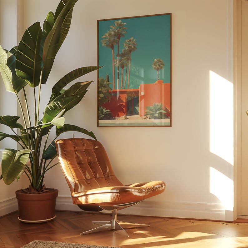 May include: A framed art print depicting a mid-century modern scene with palm trees and a coral-colored building. A brown leather chair with a chrome base sits in front of the artwork. A large potted plant is to the left.