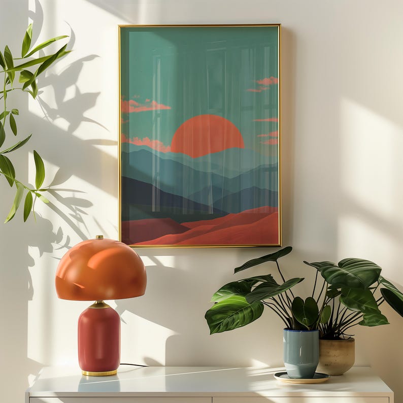 May include: A modern interior scene featuring a red and orange table lamp with a rounded shade and a framed landscape art print. The artwork depicts a sunset over layered mountains. Potted plants add a touch of nature to the decor.