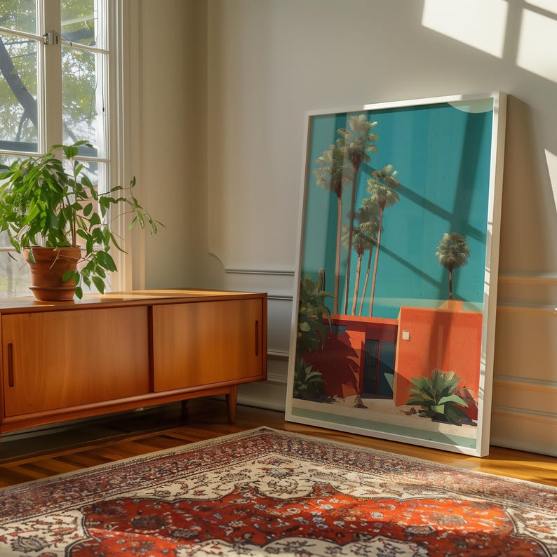 May include: A framed art print featuring a tropical scene with palm trees, a turquoise sky, and orange buildings. The artwork is leaning against a white wall in a room with a wooden cabinet, a potted plant, and a patterned rug.