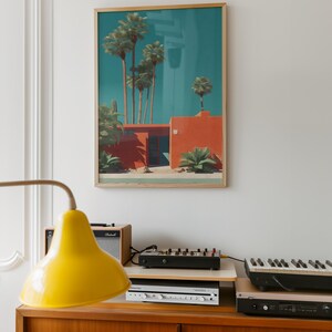 May include: A framed art print depicts a mid-century modern style building with palm trees against a teal sky. The building is a vibrant orange with a flat roof. The artwork is displayed above a wooden cabinet with a yellow lamp, audio equipment, and a keyboard.