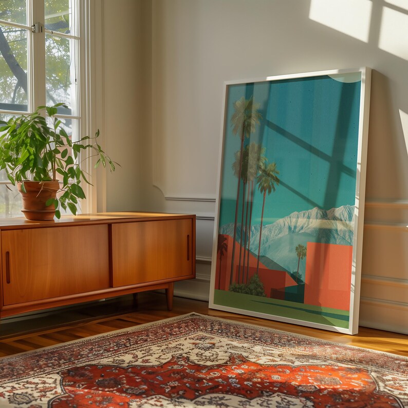 May include: A framed art print featuring a desert landscape with palm trees, mountains, and red buildings. The artwork is displayed in a bright room with a wooden cabinet, a potted plant, and a patterned rug.
