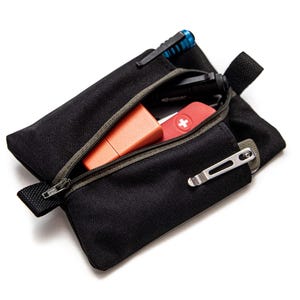 May include: A black zippered pouch with a green zipper pull. The pouch is open and contains a red first aid kit, an orange lighter, a silver multi-tool, and a blue pen.