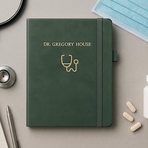 Könnte beinhalten: Ein dunkelgrünes Notizbuch mit dem Namen "DR. GREGORY HOUSE" und einem goldenen Stethoskop-Symbol. Ein Stethoskop, ein Notizblock, ein Stift, eine Gesichtsmaske, eine Pillenflasche und Pillen sind um das Notizbuch auf einer grauen Oberfläche angeordnet.
