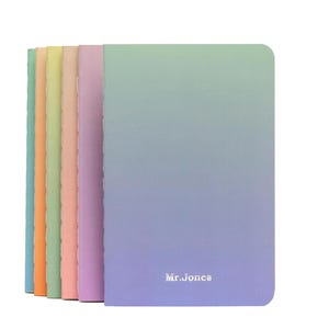 Puede incluir: Conjunto de seis cuadernos de color pastel con un diseño degradado. Los cuadernos están apilados y presentan el texto "Mr. Jones" en la parte delantera.