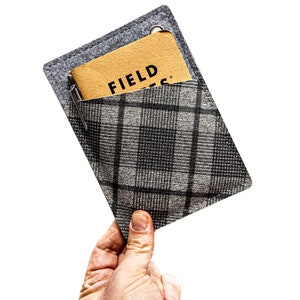 May include: A gray felt pouch with a black and white plaid pocket. A brown notebook with the text "FIELD NOTES" is inside the pocket.