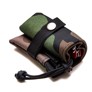 May include: A camouflage-patterned pouch with a black strap and a drawstring closure. The pouch is rolled up and secured with a button. It contains a black pen and a multi-tool.