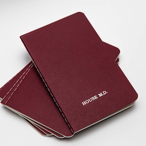 May include: A stack of burgundy notebooks with the text "HOUSE M.D." printed on the top notebook.