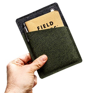 Könnte beinhalten: Eine grüne Stofftasche mit einem braunen Notizbuch und einem Stift darin. Das Notizbuch hat den Schriftzug "FIELD" auf dem Cover.