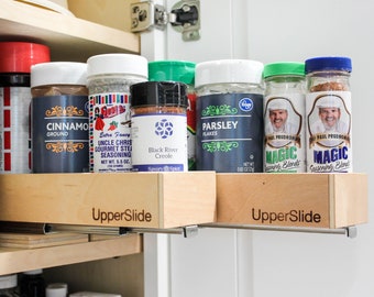 May include: A close-up of a wooden spice rack with a variety of spices in glass jars. The rack is labeled "UpperSlide" and is mounted on a wooden shelf. The spices include cinnamon, parsley, Uncle Chris Gourmet Steak Seasoning, Black River Creole, and Magic Seasoning Blends.