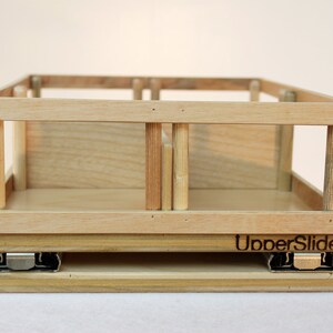 May include: A wooden drawer slide with a light wood finish. The drawer slide has a metal track and the text "UpperSlide" is printed on the front.