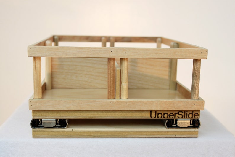 May include: A wooden drawer slide with a light wood finish. The drawer slide has a metal track and the text "UpperSlide" is printed on the front.