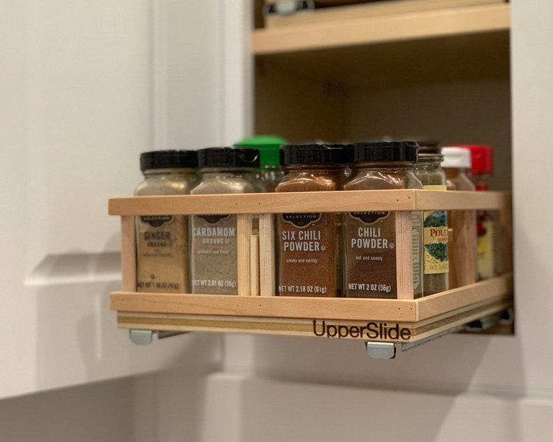 May include: A wooden spice rack with a slide-out drawer, holding various spice jars with labels like "Ginger", "Cardamom", "Six Chili Powder", and "Chili Powder". The rack is labeled "UpperSlide".
