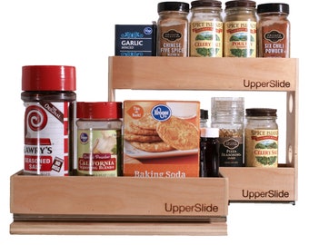 May include: A two-tiered wooden spice rack with a slide-out drawer. The top tier holds various spice jars, including Chinese Five Spice, Celery Salt, Poultry Seasoning, and Six Chili Powder. The bottom tier holds a box of baking soda, a jar of garlic powder, a jar of pizza seasoning, and a jar of celery salt. The rack is labeled "UpperSlide" on each tier.