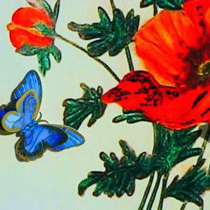 Puede incluir: Un broche de mariposa azul con bordes dorados y patrones de alas intrincados, colocado junto a una ilustraci&oacute;n impresa de vibrantes amapolas rojas con hojas de color verde oscuro sobre un fondo de color crema claro.