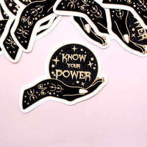 May include: A collection of stickers featuring a black hand holding a crystal ball with the words "KNOW YOUR POWER" in gold lettering. The crystal ball is set against a starry background. The stickers have a white border and are on a pink background.