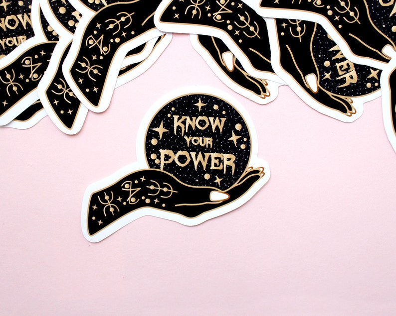 May include: A collection of stickers featuring a black hand holding a crystal ball with the words "KNOW YOUR POWER" in gold lettering. The crystal ball is set against a starry background. The stickers have a white border and are on a pink background.