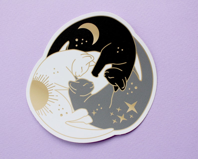 Pu&ograve; includere: Un adesivo circolare con un design yin-yang con gatti. Un gatto &egrave; nero con una luna crescente dorata, l'altro bianco con un sole dorato. Un gatto grigio al centro, con stelle e dettagli dorati.