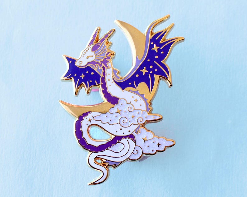 May include: A purple and white enamel pin of a dragon curled around a crescent moon. The dragon has a white body with purple accents and a gold crescent moon. The dragon's wings are spread out and have a purple and gold design.