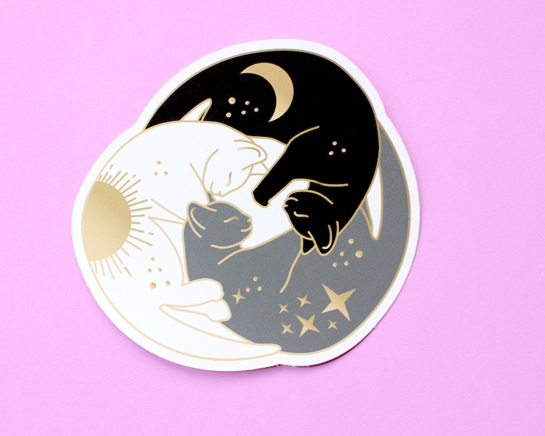 Pu&ograve; includere: Un adesivo fustellato con un design Yin e Yang con gatti. Il design include un gatto nero con una luna dorata, un gatto bianco con un sole dorato e un gatto grigio con stelle dorate. L'adesivo ha un bordo bianco ed &egrave; posto su uno sfondo rosa.