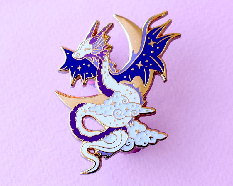 May include: A gold-tone enamel pin featuring a purple and white dragon curled around a crescent moon with stars. The dragon has a blue and white body with a purple tail and wings.
