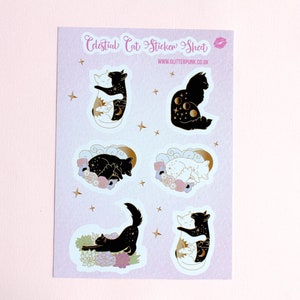May include: A sheet of stickers featuring celestial cat designs. The stickers are on a light purple background with gold stars. The designs include a black cat with a crescent moon and stars, a white cat with a sun and stars, a black cat sleeping with flowers, a white cat sleeping with flowers, a black cat stretching with flowers, and a white cat hugging a black cat with a sun and moon.