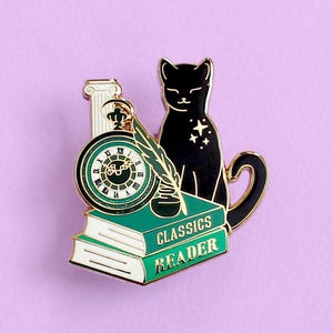 May include: Enamel pin featuring a black cat with star accents, a pocket watch, a quill and ink, and two green books with the words "CLASSICS READER". The pin has gold accents and a purple background.
