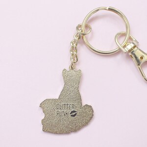 May include: Gold-colored keychain with a cat-shaped charm. The charm has the text "GLITTER PUNK" and a lipstick kiss mark. The keychain includes a split ring, a chain, and a lobster clasp for easy attachment.