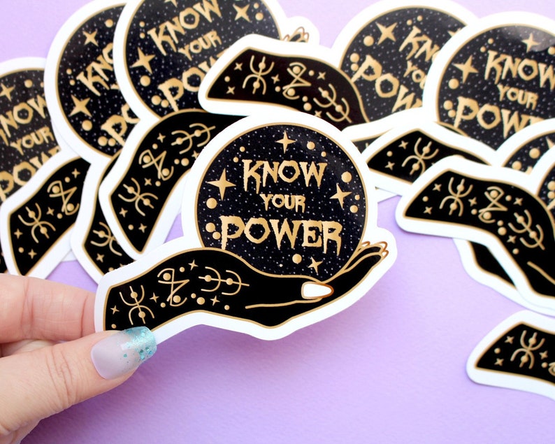 May include: A collection of stickers featuring a black hand holding a crystal ball with the words "KNOW YOUR POWER" in gold lettering. The crystal ball is set against a starry background. The stickers have a white border.