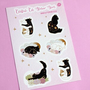 May include: A sheet of stickers featuring celestial cat designs. The stickers are white with gold outlines and feature black and white cats with celestial elements like moons and stars. The text "Celestial Cat Sticker Sheet" and "www.glitterpunk.co.uk" is printed on the sheet.