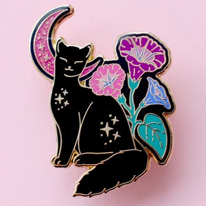 May include: Black cat enamel pin with a crescent moon and floral design. The pin features a black cat with star accents, a pink glitter moon, and purple, pink, and blue morning glory flowers. The pin has a gold border.