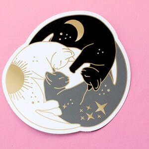 Pu&ograve; includere: Un adesivo con un design Yin e Yang con gatti. Il design include un gatto bianco con un sole dorato, un gatto nero con una luna dorata e un gatto grigio al centro. Sono incluse anche stelle e punti dorati.