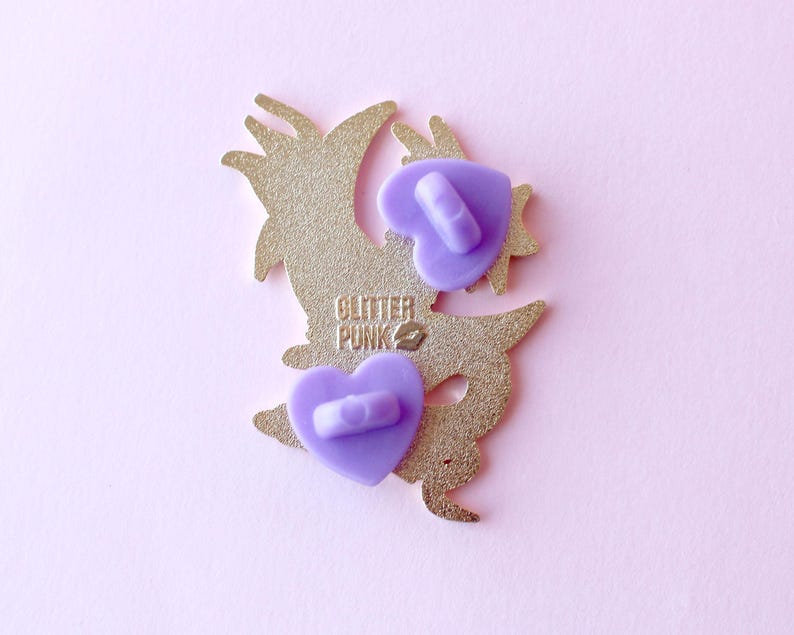 May include: Gold-colored enamel pin featuring a cartoon dragon with a purple heart on its chest. The pin has two purple butterfly backings and the text "Glitter Punk" on the back.