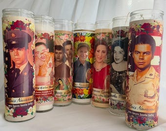May include: A collection of glass jar candles with portraits of people and floral designs. The candles feature images of individuals in various settings, with text in Spanish. The candles are arranged on a white surface.