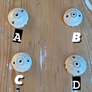May include: Six white ceramic ceiling fixture covers with decorative floral designs. The covers are labeled A through G.