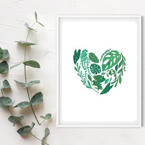 May include: A white framed print with a green heart made of various leaves and foliage. The heart is centered on a white background.