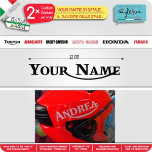 May include: A black and white sticker with the text "YOUR NAME" in a curved font. The sticker is 12 cm wide and is shown on a red motorcycle helmet with the name "ANDREA" in a similar font.