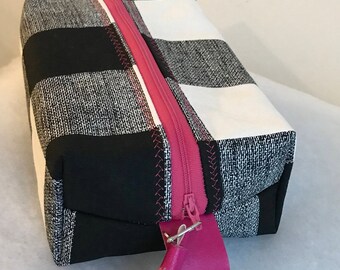 May include: Black and white checkered zippered pouch with a pink tassel. The pouch is made of a textured fabric.