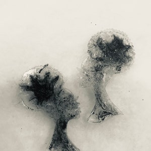 May include: A pair of black and white resin earrings featuring a silhouette of a woman's face with an afro hairstyle.