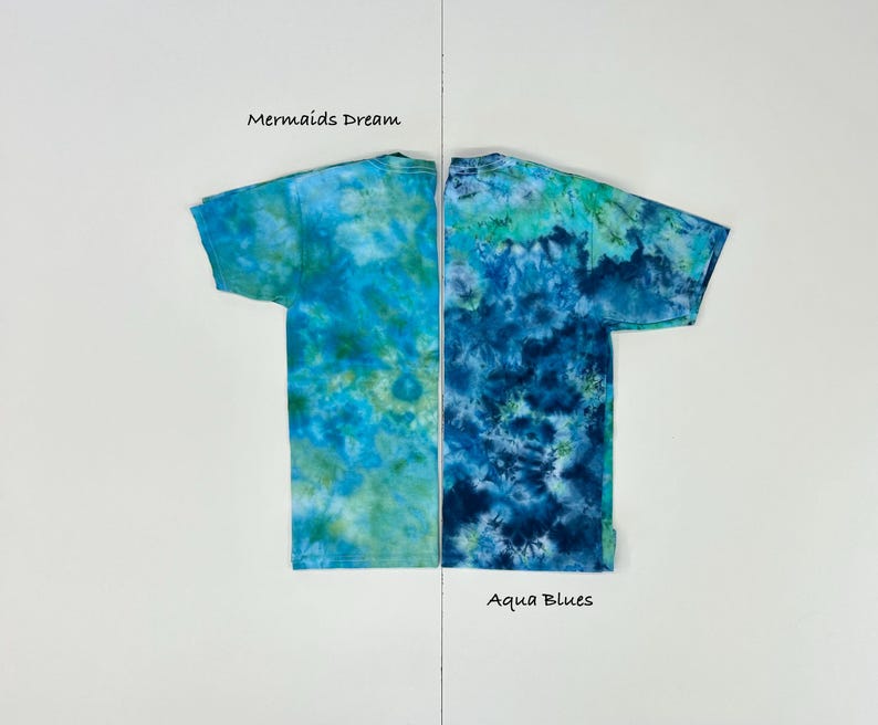 May include: Two tie-dye t-shirts, side-by-side, each with a unique blue and green pattern. The left shirt is labeled "Mermaids Dream," and the right shirt is labeled "Aqua Blues." Both shirts have short sleeves and a crew neck.