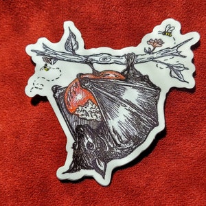 May include: A sticker featuring a detailed illustration of a bat hanging upside down from a tree branch. The bat is black and white with orange accents. Two bees and small flowers are also depicted on the branch. The sticker has a white border.