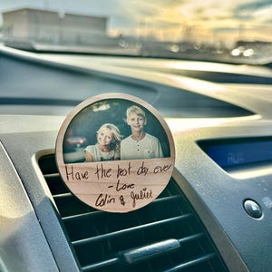 May include: A wooden car air freshener with a photo of two people and the text "Have the best day ever - love Colin & Juliet" engraved on it.