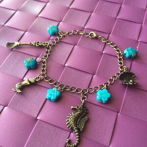 May include: A gold chain bracelet with turquoise blue charms, including a seashell, a starfish, a trident, a seahorse, and flowers.