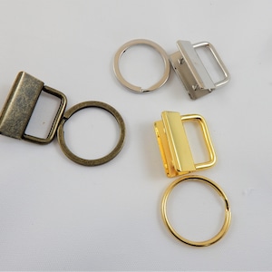 May include: Three key rings with different finishes: antique brass, gold, and silver. Each ring has a square-shaped swivel clasp.