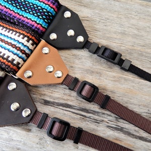 May include: Three camera straps with different coloured woven fabric and leather accents. Each strap has a black plastic adjustable buckle.