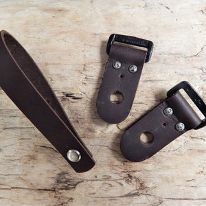 May include: Three brown leather straps with metal buckles. Two straps have a hole and two metal rivets. The third strap has a single metal rivet.
